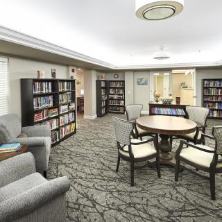 A cozy library area with bookshelves, a round table surrounded by chairs, and comfortable seating.