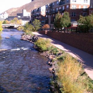 A scenic view of an urban river with a pathway and buildings along the shoreline.