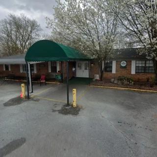 A building entrance with a green awning and surrounding trees in bloom.