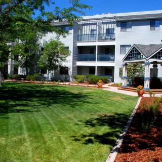 A view of a residential apartment building with well-maintained landscaping and a lush green lawn.