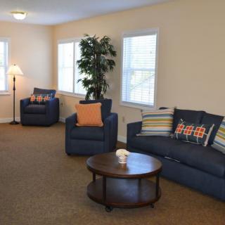 A cozy living room with blue sofas, a round coffee table, and natural lighting from multiple windows.