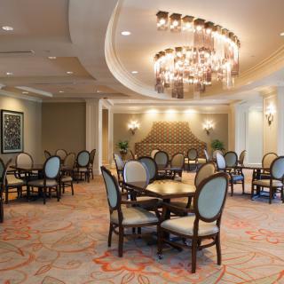 An elegant dining room with upholstered chairs, round tables, and a decorative chandelier.
