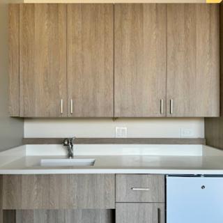 A minimalist kitchen setup with wooden cabinets, a sink, and a small refrigerator.