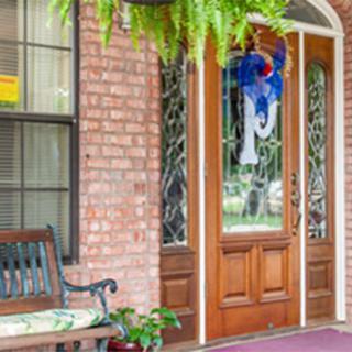 A welcoming front porch with a wooden door, brick exterior, and decorative elements including a bench and hanging plants.