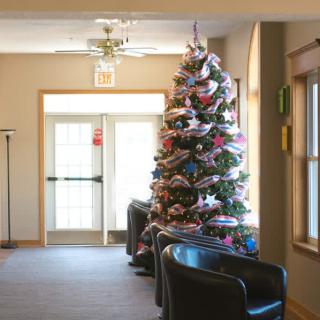 A festively decorated Christmas tree stands in the lobby, surrounded by chairs and lit by natural light from nearby windows.