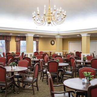 An elegant dining room with multiple tables and chairs, highlighted by a large chandelier.