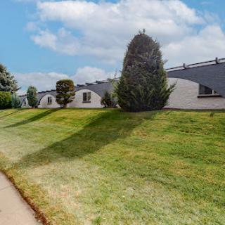 A peaceful landscape featuring well-maintained grass, trees, and modern buildings under a clear sky.
