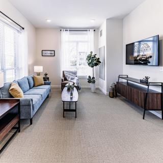 A modern and spacious living room featuring a comfortable sofa, sleek coffee table, and a mounted television, with ample natural light streaming through large windows.