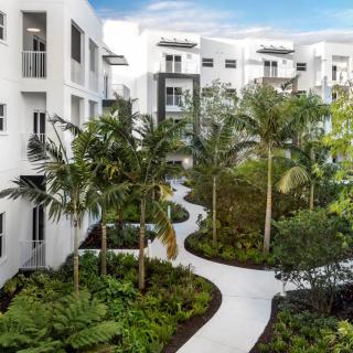 Modern apartment complex with tropical landscaping and winding pathways.