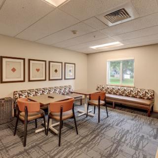 A cozy dining area featuring simple furniture, framed art on the walls, and a view through the window.