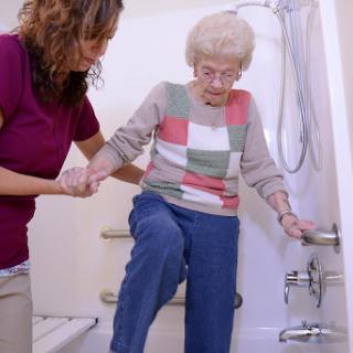 A caregiver helps an elderly woman safely enter the shower.
