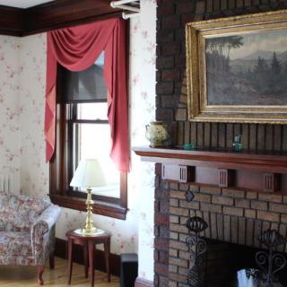 A cozy living room featuring a brick fireplace, adorned with a framed painting and red curtains.
