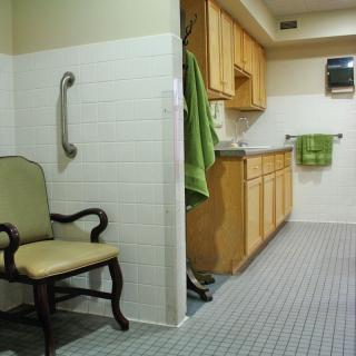 A combined kitchen and bathroom area with wooden cabinets, a tiled floor, and green towels.