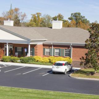 A suburban building with a brick exterior and an adjacent parking lot containing a white car.
