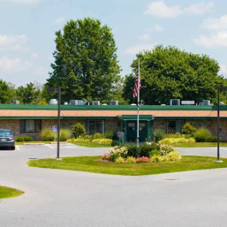 A view of a single-story building surrounded by lush greenery and a flag waving in the background.