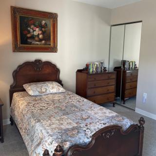 A cozy bedroom with a single vintage-style bed, a dresser with a mirror, and a floral painting on the wall.