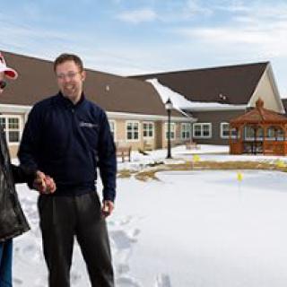 Two men shaking hands in a snowy outdoor setting near residential buildings.