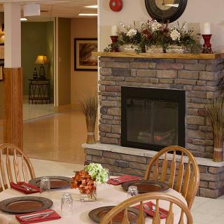 A cozy dining area featuring a stone fireplace and neatly set tables with wooden chairs.
