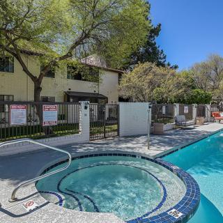 An outdoor pool area with a hot tub next to an apartment building on a sunny day.