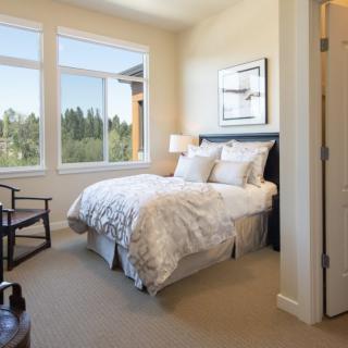 A cozy and bright bedroom with a neatly made bed and large windows overlooking greenery.
