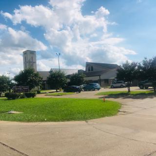 A view of a building with a grassy area and scattered clouds in the sky.