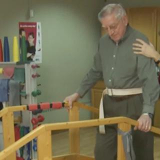 An elderly man receiving support during a physical therapy session.