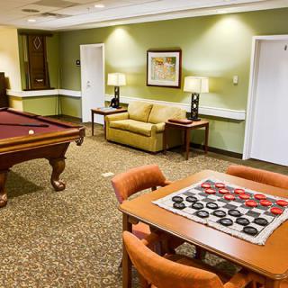 A cozy game room featuring a billiards table and a checkers board on a table, with comfortable seating for relaxation.