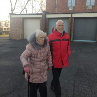 An elderly woman walking with a man, both dressed for winter.