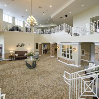 A spacious and elegantly designed lobby with a chandelier, featuring carpeted flooring and stylish railings.