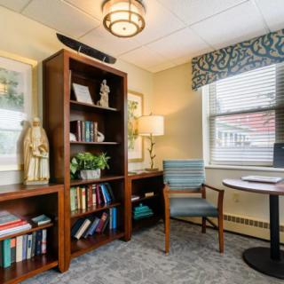 A cozy office space with a bookshelf, armchair, and window providing natural light.