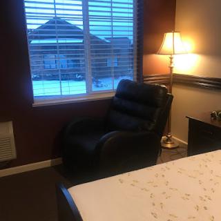 A cozy bedroom setting featuring a recliner chair, lamp, and a view out the window.