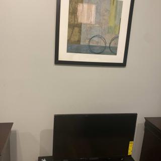 A framed abstract painting hangs on the wall above a television set placed between two pieces of furniture.