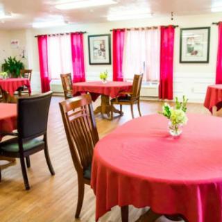A brightly lit dining room with tables covered in red tablecloths and decorated with small flower arrangements.