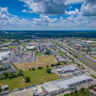 A panoramic aerial view of an industrial zone with low-rise buildings and a highway under a partly cloudy sky.