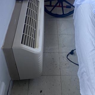 A hotel room with an air conditioning unit next to a bed and a wheelchair.