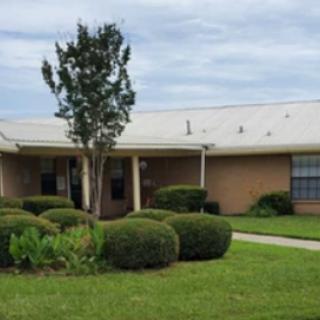 A well-maintained single-story building surrounded by lush greenery and a cloudy sky.