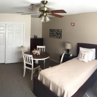 A cozy bedroom with a single bed, round table, and chairs under a ceiling fan.