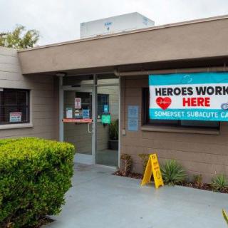 Entrance to a healthcare facility with a 'Heroes Work Here' banner displayed.