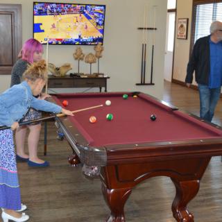 Children playing pool in a game room while a basketball game is shown on the television.