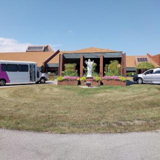 A view of a facility featuring transportation vehicles parked outside, with a landscaped area and a statue.