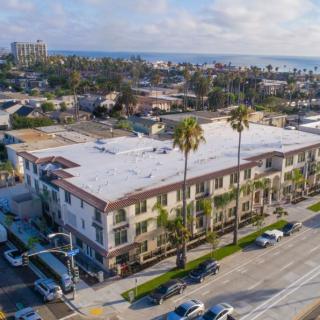 Aerial view of a coastal urban area with palm trees lining the streets and a large building in the foreground.
