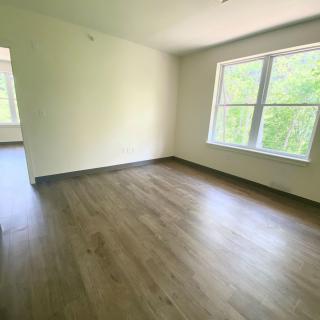 An empty room with hardwood flooring and a large window letting in natural light.