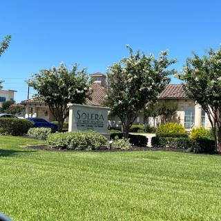 A well-maintained residential community sign surrounded by lush greenery and a clear blue sky.