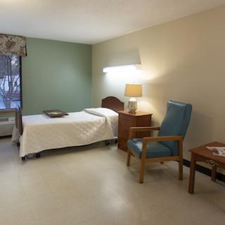 A simple and clean patient room with a single bed, a chair, and natural light coming from the window.