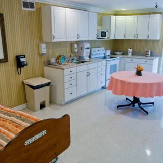 A hospital room featuring a kitchenette with cabinets, a round table, and a bed.
