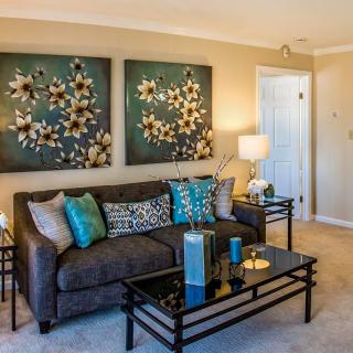 A stylish living room featuring a comfortable sofa adorned with colorful cushions, two floral artworks on the wall, and a modern glass coffee table.