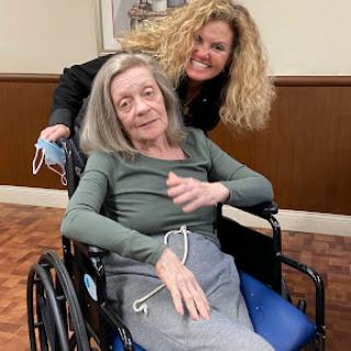 A joyful moment shared between a caregiver and an elderly woman in a wheelchair.