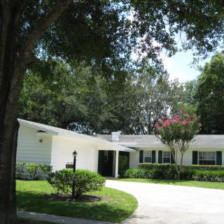 A single-story suburban house with a curved driveway and surrounding trees.