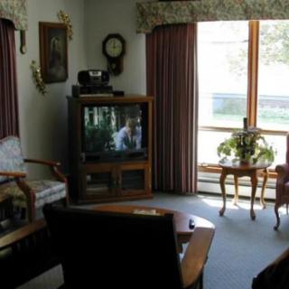 A vintage-style living room with a television, furniture, and curtains by a large window.