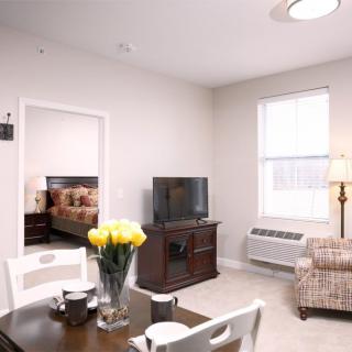 A cozy living room with a dining area, featuring a television, table with flowers, and comfortable seating.